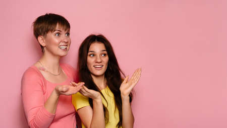 A studio shot of two young girl friends on a bright background with surprised emotions on their face. A place for your text or advertisement.の写真素材