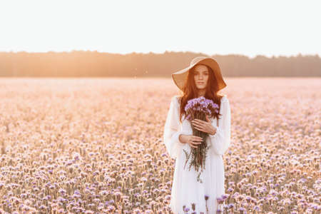A beautiful girl in a lavender field. A beautiful woman in the style of provence in a white dress with a bouquet in her hands.の写真素材