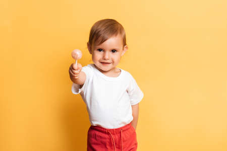 A little girl is eating a sweet lollipop on a stick. Yellow background. The concept of prevention of caries and diabetes in children.の写真素材