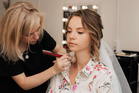 Shooting in a beauty salon. makeup artist makes a wedding makeup for a young girl.の写真素材