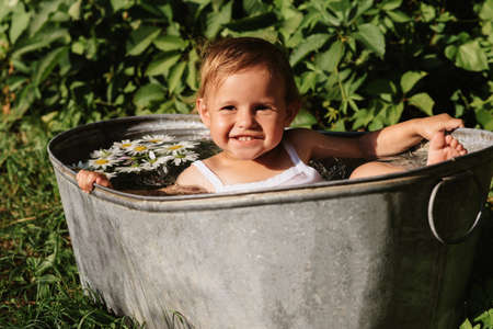 A baby smiling girl is bathing in a bathtub standing in the garden, on a hot sunny summer dayの写真素材