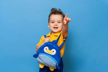 Cute little one cuddles with his backpack on a blue background. Funny kidの写真素材