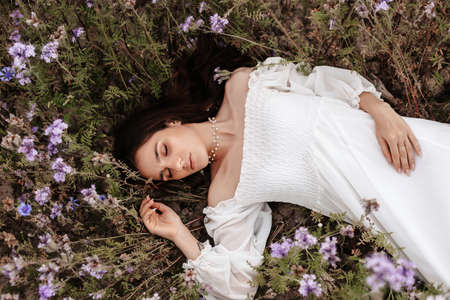 A young beautiful girl lies with her eyes closed in a blooming field of Provence. Romantic atmosphereの写真素材