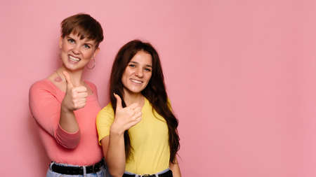 A studio shot of two young girl friends on a bright background shows an approving hand sign. A place for your text.の写真素材