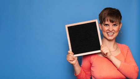 Studio shot of a smiling young woman holding a blank letter board on a blue background. Copy space,...