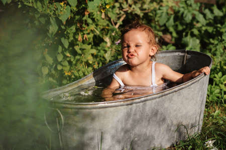 A baby smiling girl is bathing in a bathtub standing in the garden, on a hot sunny summer dayの写真素材