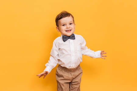 A studio shot of a cute little boy grimacing stands on a yellow background. Funny kidの写真素材