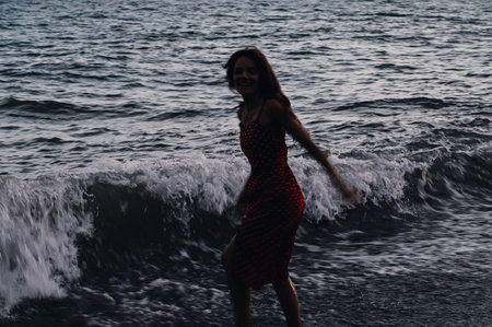 A young girl in a dress runs along the coastline on the waves on a summer evening. The concept of...