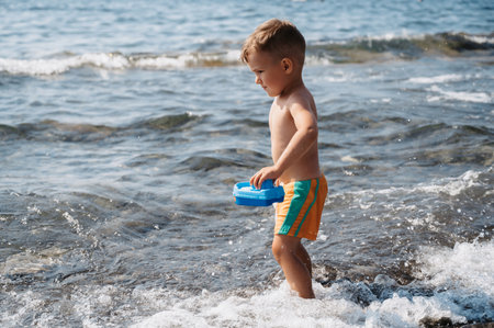 A cute Caucasian boy launches a plastic boat into the sea. Active holidays on the coastの写真素材