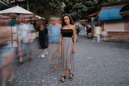 A crowd of moving blurry tourists walking past a young beautiful girl standing in the square. Vacation at the resort. Tourism.の写真素材