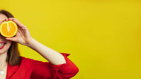 Portrait of a Caucasian girl with a radiant clean skin holding orange halves isolated on a yellow...