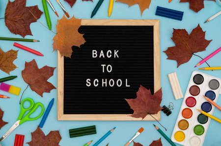 Text: Back to school soon on a wooden letter board. buying stationery, flat, bright background. Maple leaves. Autumn school fees.の写真素材