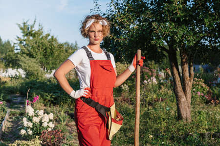 A happy female gardener in gloves and an apron stands against the background of a flower bed in a home garden . Gardening and floriculture. Flower careの写真素材