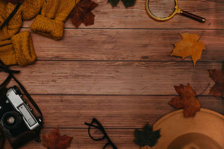 Frame of autumn accessories, flatlay. Hat, sweater, leaves maple, glasses, retro camera on wooden background. Copying spaceの写真素材
