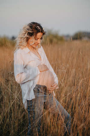 A happy future young mother is a woman in white clothes with a big pregnant belly. Natural landscape. The concept of pregnancy.の写真素材