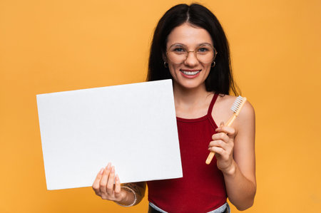 A smiling woman with healthy teeth is holding a toothbrush and a clean empty banner. A young beautiful girl on a bright isolated background. Oral hygiene. A place for your text.の写真素材
