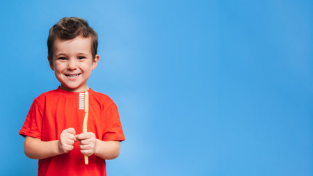 A smiling boy with healthy teeth holds a toothbrush on a blue isolated background. Oral hygiene. A place for your text.の写真素材