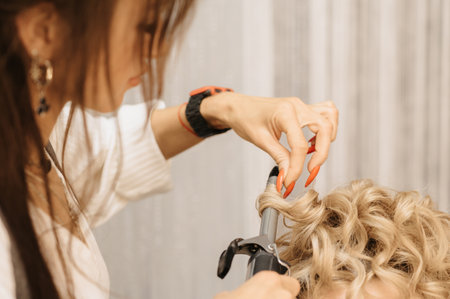 Shooting in a beauty salon. A hair stylist makes a hairstyle for a young dark-haired girl with the help of a hair styler.の写真素材