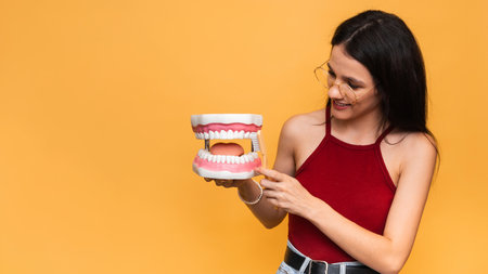 A smiling woman with healthy teeth cleans the shape of the jaws with a toothbrush on a yellow...