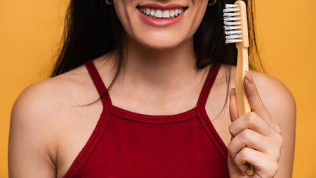 A smiling woman with healthy teeth holds a toothbrush in her hands. A young beautiful girl on a bright isolated background. Oral hygiene.の写真素材
