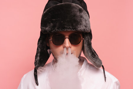 A Russian man in a traditional hat smokes a hookah and enjoys it. Pink backgroundの写真素材