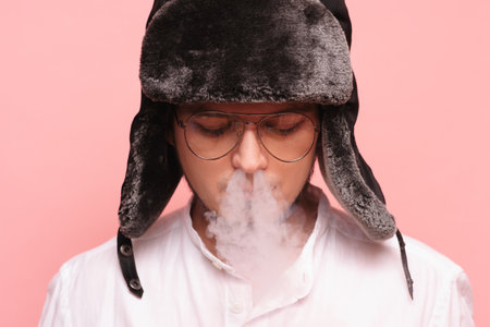 A Russian man in a traditional hat smokes a hookah and enjoys it. Pink backgroundの写真素材