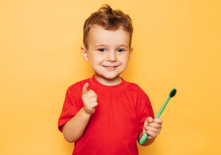 The happy kid is holding a toothbrush on a yellow background and smiling showing his teeth. Health care, oral hygieneの写真素材