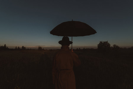 surreal silhouette of a man in a suit with an umbrella, standing in a raincoat in a field. The concept of freedomの写真素材