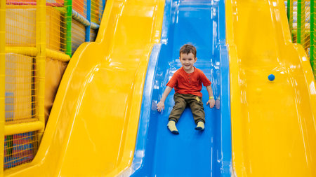 A boy rides from the childrens slides on the playground in the play center. Active leisure. Childhood and joy.の写真素材