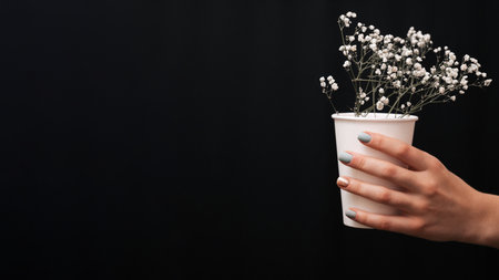A womans hand with a neat manicure holds a plastic cup with flowers inside. A place for your text or advertisement.の写真素材