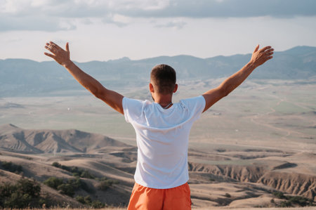 A young man stands with his hands up in the fresh air in a mountainous area.