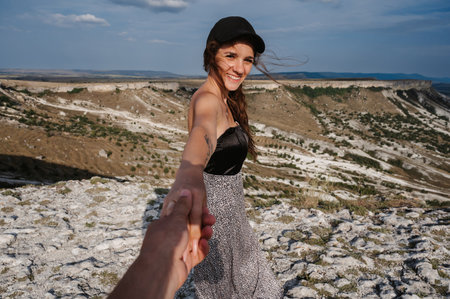 follow me with a young woman guiding a traveler by the hand into a mountainous area. Mountain landscape under the skyの写真素材