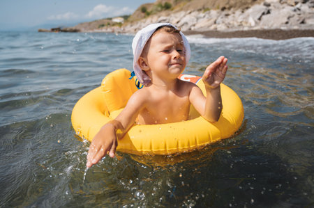 Baby boy splashes water in the sea, floating in a yellow inflatable circle. The kid is having fun and fooling aroundの写真素材