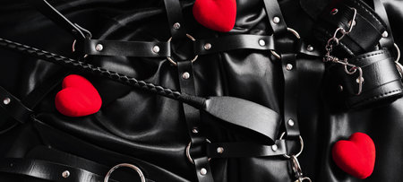 Explore the world of kinky play. Top view of bdsm leather kit against of a black silk. Horizontal wide photo subtitle, cover. copy-spaceの写真素材