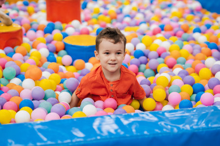 Portrait of a happy little boy jumping merrily into a dry pool with colorful balloons. A toddler boy is playing and having a good time at the childrens entertainment center.の写真素材