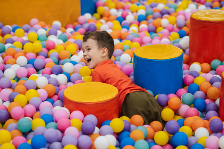 A happy little boy has fun jumping into a dry pool with colorful balls. The kid boy is playing and having a good time in the game room with colorful balls.の写真素材