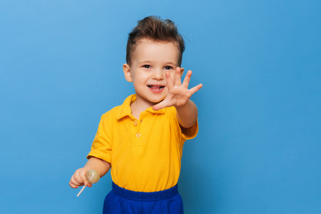 Baby boy with lollipop stands on a blue wall background. Prevention of childhood caries.の写真素材