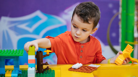 Educational toys. The picture is a plan of a boys child playing with colorful plastic bricks at a table. The kid has fun and builds from bright constructor cubes. Early learning.の写真素材