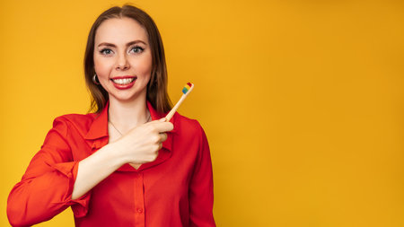 A happy woman takes care of her teeth and holds a toothbrush A young lady brushes her teeth A beautiful Caucasian girl has beautiful teeth. Yellow background, copying space. Dental careの写真素材