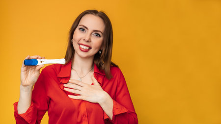 Studio shot of an emotional young woman with a positive pregnancy test in her hands. An expression of surprise and joy on his face. The concept of pregnancy, motherhood. A place for your text.の写真素材