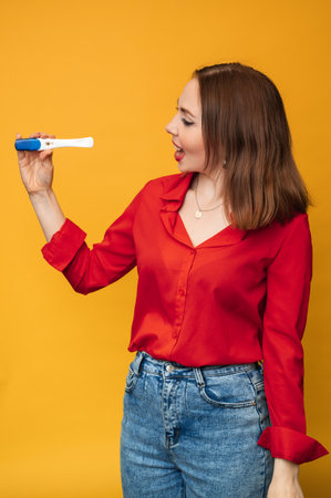 Studio shot of an emotional young woman with a positive pregnancy test in her hands. An expression of surprise and joy on his face. The concept of pregnancy, motherhood.の写真素材