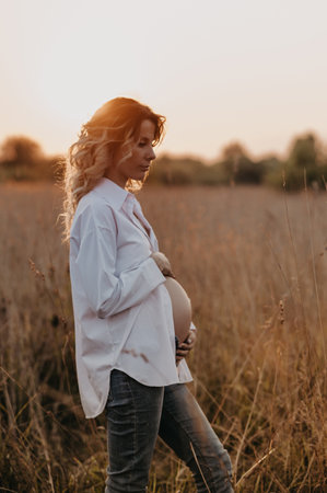 The silhouette of a young expectant mother in the setting sun in a natural landscape. The concept of calm in pregnancy. Third trimester.の写真素材