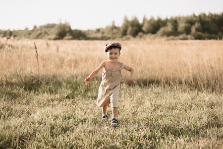 The boy-child is having fun and actively running in the field. A cheerful and sincerely rejoicing boy. Childhood in the countryside.の写真素材