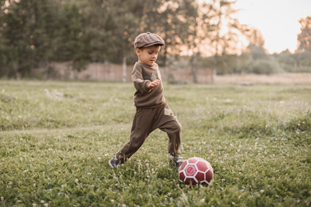 A boy is playing football in the countryside. The joyful childhood of the baby. Active sports.の写真素材