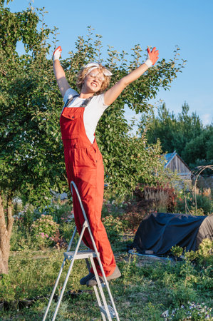 Portrait of a young woman gardener. A worker in a garden with ornamental plants standing on a stepladder.Gardening and floriculture. Growing flowers in the home garden.の写真素材