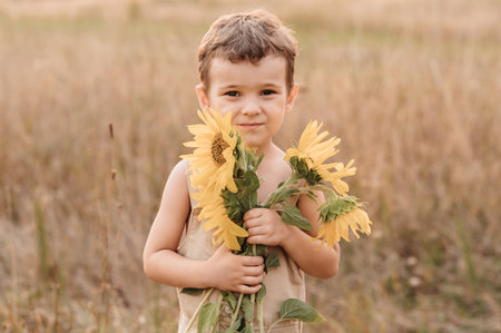 A cute little laughing boy in a field of sunflowers, holding a huge bouquet of flowers in his hands on a sunny summer evening. The golden hour.の写真素材