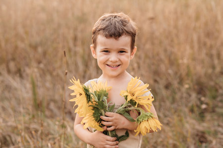 A cute little laughing boy in a field of sunflowers, holding a huge bouquet of flowers in his hands on a sunny summer evening. The golden hour.の写真素材