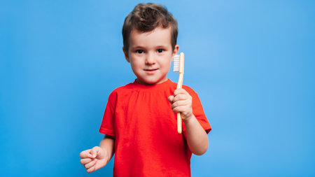 A smiling boy with healthy teeth holds a toothbrush on a blue isolated background. Oral hygiene. A place for your text.の写真素材