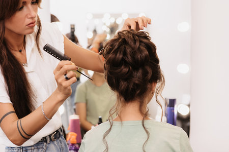 Shooting in a beauty salon. A hair stylist corrects the hairstyle of a young dark-haired girl with a hair comb.の写真素材