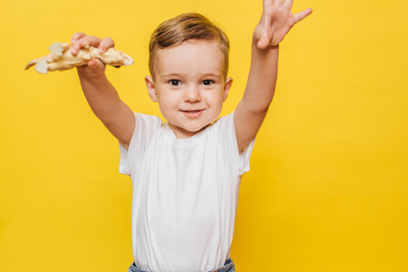 Cute laughing little boy on a yellow background with a dinosaur toy in his hands.の写真素材